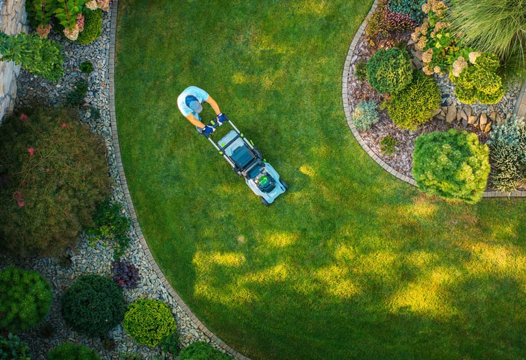 A person mows a lush green lawn in a beautifully landscaped garden