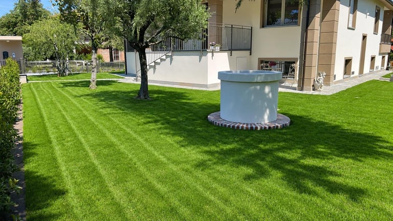 Well-manicured residential lawn with diagonal stripe pattern, metal storage tank, mature trees, and modern house with patio in background