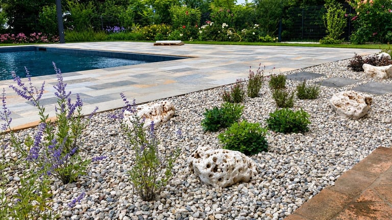 Modern pool deck with white gravel landscaping, purple flowering plants, and green shrubs surrounding a swimming pool