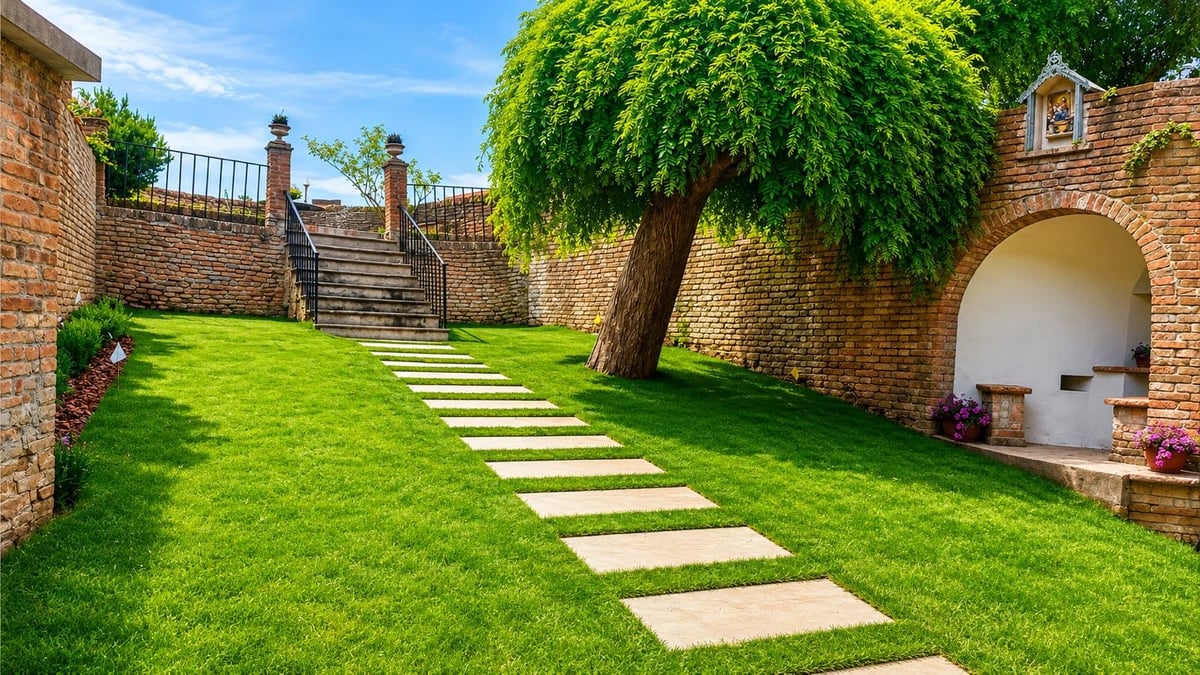 Lush green garden courtyard with stepping stone path, brick walls, large tree, and archway entrance under blue sky